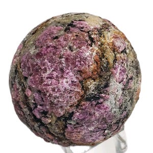 Könnte beinhalten: Nahaufnahme eines kugelförmigen Mineralexemplars mit rauer Textur. Der Stein weist eine Mischung aus Farben auf, darunter tiefes Rosa, Braun, Grau und Beige. Die Oberfläche ist uneben, mit sichtbaren kristallinen Strukturen.