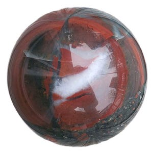 Può includere: Una gemma sferica lucidata con un mix di colori rosso, nero, bianco e grigio. La pietra ha un aspetto marmorizzato con motivi a vortice e una finitura lucida. La gemma è un oggetto decorativo.