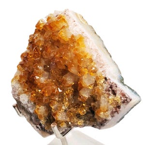 May include: A cluster of citrine crystals, showcasing a vibrant display of golden-yellow hues. The crystals are densely packed, with a rough, textured surface. The base of the cluster has a mix of white, brown, and gray tones.