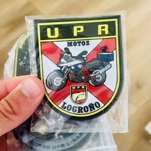 May include: A patch featuring a motorcycle graphic with the text "UPR MOTOS LOGRO&Ntilde;O". The patch has a black border, a red and white background, and the text "UPR" in yellow.