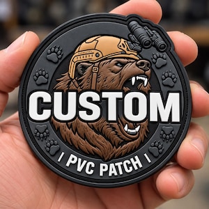 May include: A circular black PVC patch featuring a brown bear wearing a tan tactical helmet with night vision goggles. The bear is snarling with visible teeth. The text CUSTOM is in large white letters, with PVC PATCH in smaller white letters below.