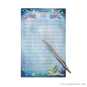 May include: A blue and white notepad with a whimsical design featuring flying cats with wings and stars. The notepad has the words "things to do" written on it.