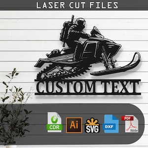 May include: Black metal wall art featuring a snowmobile with a rider, set against a white and gray wood-paneled background. The text "LASER CUT FILES" is at the top, and "CUSTOM TEXT" is at the bottom. Includes file type icons.
