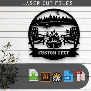 May include: Black and white laser cut file design of a campfire scene with two chairs and a lake in the background. The design includes the text "CUSTOM TEXT".