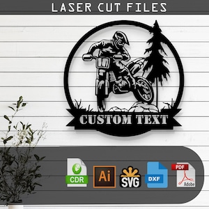 May include: Black and white silhouette of a motocross rider jumping over a hill with a pine tree in the background. The design is in a circle with the text "CUSTOM TEXT" on a banner below. The image is for laser cutting files.