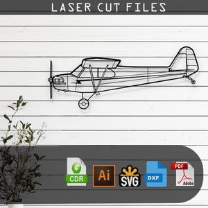 Puede incluir: Un dibujo en blanco y negro de un avión pequeño, un Piper Cub, sobre un fondo de madera blanca. La imagen incluye el texto "LASER CUT FILES" en la parte superior y los iconos para los formatos de archivo CDR, AI, SVG, DXF y PDF en la parte inferior.