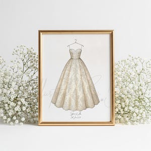 May include: A framed illustration of a strapless wedding dress with a full skirt, detailed with lace patterns. The artwork is in a gold frame, with the names "Stephanie & Ann" and the date "3rd June 2029" at the bottom. The background is white.