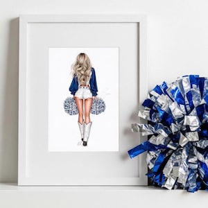 May include: A framed illustration of a cheerleader in a blue top, white shorts, and white boots, holding blue and silver pom-poms. The artwork features long blonde hair and is set against a white background. A pom-pom rests on the right.