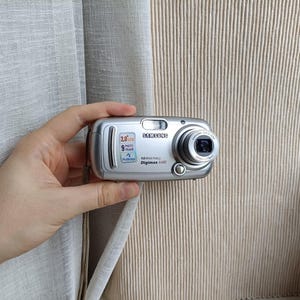 May include: A silver Samsung Digimax 430 digital camera featuring a 2.0 inch LCD screen, a 4.0 mega pixel sensor, and a lens with 3x optical zoom. The front of the camera displays the brand name, model number, and PictBridge logo in black text.