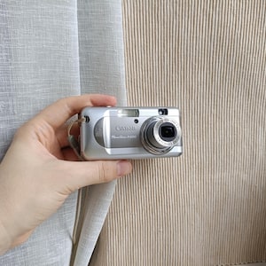 以下が含まれることがあります： シルバーのキヤノンPowerShot A820デジタルカメラ。4.0メガピクセルのラベル、内蔵フラッシュ、および前面に「Canon Zoom Lens 5.4-17.3mm 1:2.8-5.5」と印字された伸縮式レンズを備えた、コンパクトな長方形のデバイスです。
