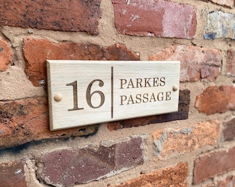 May include: A wooden house number sign with the number 16 and the text "Parkes Passage" engraved on it. The sign is mounted on a brick wall.