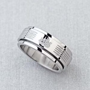 K&ouml;nnte beinhalten: Ein silberfarbener Ring mit ge&auml;tzten Mustern und einem drehbaren Au&szlig;enband. Der Ring weist detaillierte Designs auf, m&ouml;glicherweise religi&ouml;ser oder kultureller Natur, was eine einzigartige &Auml;sthetik verleiht. Der Ring wird auf einer hellgrauen Oberfl&auml;che gezeigt.
