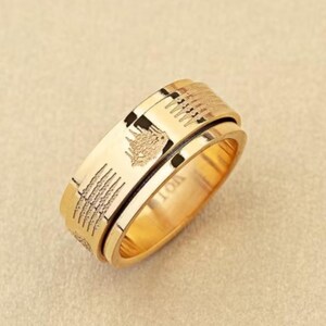 K&ouml;nnte beinhalten: Ein goldfarbener Ring mit eingravierten Details. Der Ring hat ein zentrales Band mit strukturiertem Design und ein sich drehendes &auml;u&szlig;eres Band. Der Ring hat ein eingraviertes Bild eines Wolfes. Das Wort "TON" ist auf dem Ring eingraviert.