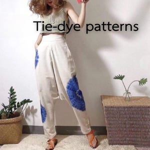 Op de afbeelding: Crèmekleurige broek met blauwe tie-dye patronen. De tekst "Tie-dye patterns" wordt op de afbeelding weergegeven. De broek heeft een relaxte pasvorm en wordt gedragen met een beige crop top. Het model draagt oranje sandalen.