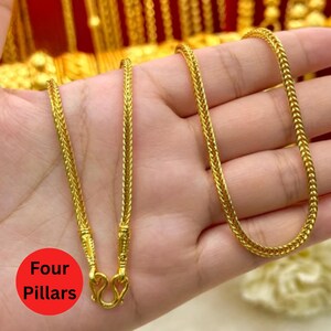 May include: Close-up of three gold-colored necklaces with intricate woven chain designs. The necklaces are displayed on a hand, showcasing their texture and shine. The image is well-lit, highlighting the details of the jewelry.
