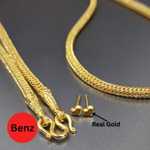 May include: A gold necklace with a woven chain design and a decorative clasp. The image also shows a pair of small heart-shaped gold stud earrings. The text "Real Gold" is next to the earrings.