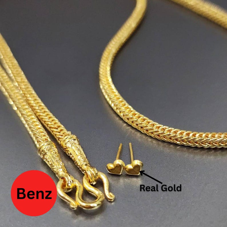 May include: A gold necklace with a woven chain design and a decorative clasp. The image also shows a pair of small heart-shaped gold stud earrings. The text "Real Gold" is next to the earrings.