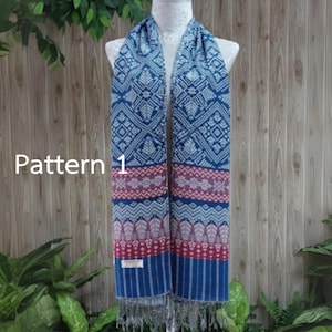 Pode incluir: Lenço azul com um padrão geométrico detalhado, exibido em um manequim. O lenço apresenta uma combinação de desenhos azuis, vermelhos e brancos, com bordas franjadas. O texto "Pattern 1" é visível.