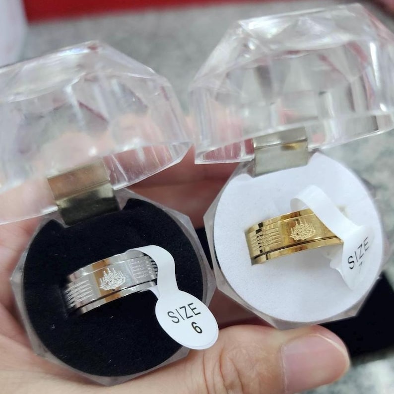 K&ouml;nnte beinhalten: Zwei Ringe, einer silberfarben und einer goldfarben, jeweils mit einem Schiffsdesign. Die Ringe werden in transparenten, facettierten Boxen mit Gr&ouml;&szlig;enetiketten pr&auml;sentiert. Der silberne Ring befindet sich in einer schwarzen Box, der goldene Ring in einer wei&szlig;en Box.