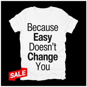 May include: White t-shirt with the text "Because Easy Doesn't Change You" in black. A red "SALE" tag is in the lower left corner. The shirt is displayed against a black background.