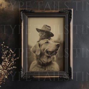 May include: Sepia-toned framed print featuring a Golden Retriever with a cat wearing a hat. The print is in a black ornate frame, displayed above a black table with a vase of dried flowers. The image has a vintage aesthetic.