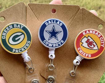 May include: Three circular badge reels featuring NFL team logos. The left reel displays the Green Bay Packers logo, the center reel shows the Dallas Cowboys star logo, and the right reel features the Kansas City Chiefs logo on a red background.
