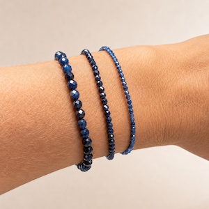 May include: Three bracelets made of faceted blue beads in varying sizes. The first bracelet features large, dark blue beads, the second has medium-sized blue beads, and the third consists of very small, delicate blue beads, all worn together.