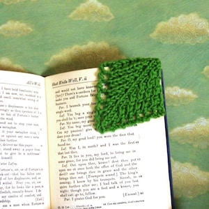 May include: A green knitted bookmark with a decorative stitch pattern. The bookmark is placed on an open book with text about Fortune and a character named Lafes.