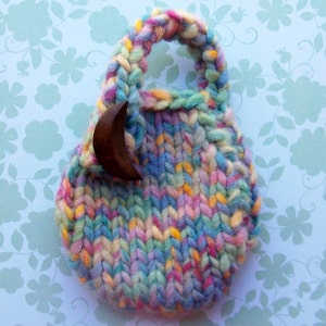 May include: A small, colorful knitted bag with a wooden crescent moon charm. The bag is made with a variety of yarn colors, including pink, blue, green, and yellow.