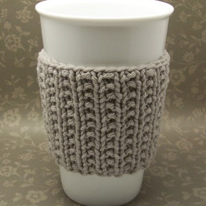 Peut inclure: Une tasse en céramique blanche avec un manchon en tricot beige. Le manchon est réalisé avec un motif de point simple.