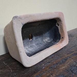 Puede incluir: Un peque&ntilde;o macetero rectangular de terracota con interior negro. El macetero tiene un agujero de drenaje en la parte inferior.
