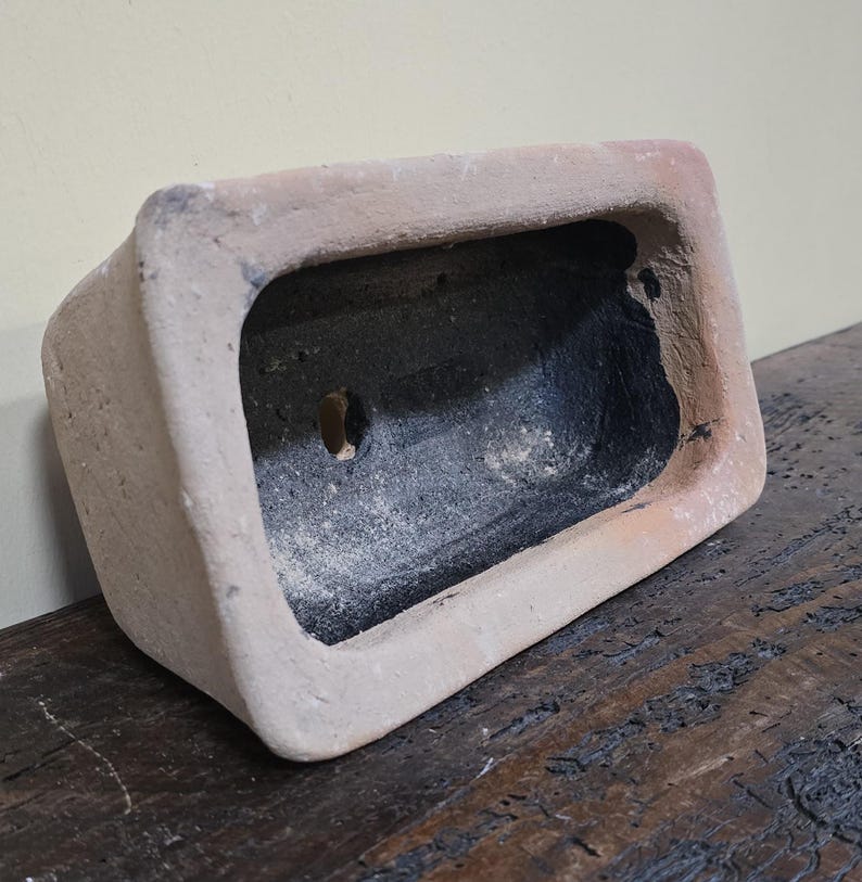 Puede incluir: Un peque&ntilde;o macetero rectangular de terracota con interior negro. El macetero tiene un agujero de drenaje en la parte inferior.