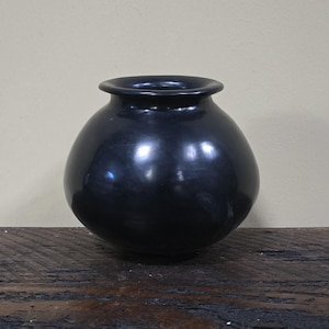 May include: A black ceramic vase with a rounded body and a slightly flared rim.