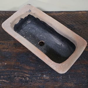 Puede incluir: Un macetero rectangular de terracota con un interior esmaltado negro. El macetero tiene un agujero de drenaje en el fondo.