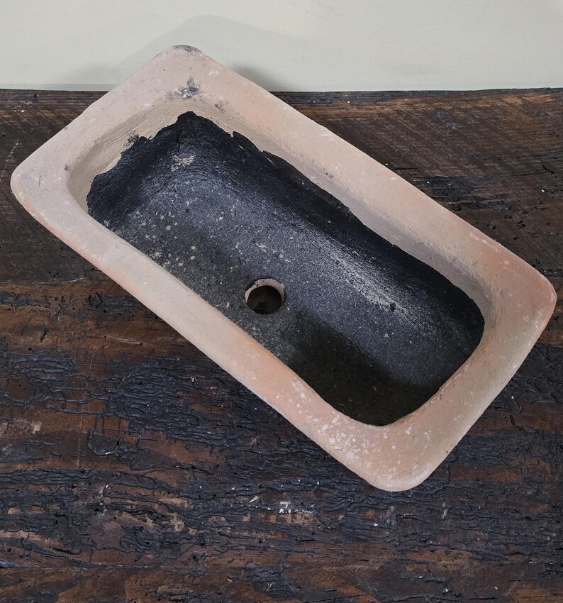 Puede incluir: Un macetero rectangular de terracota con un interior esmaltado negro. El macetero tiene un agujero de drenaje en el fondo.