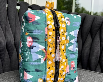 May include: A green and yellow quilted makeup bag with a zipper closure. The bag features a colorful print of mountains, trees, and camper vans.