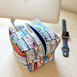 May include: A rectangular zippered pouch with a white background and a colorful pattern of license plates from different states. The pouch is open and the inside is lined with a light blue fabric.