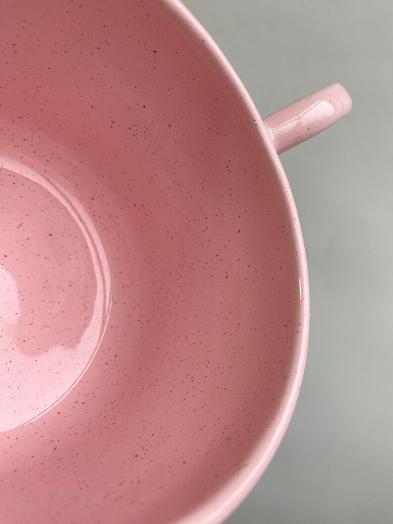 K&ouml;nnte beinhalten: Nahaufnahme einer rosa Keramiksch&uuml;ssel mit Henkel. Die Sch&uuml;ssel hat eine gesprenkelte Textur und eine gl&auml;nzende Oberfl&auml;che. Der Henkel ist eine kleine, gebogene Verl&auml;ngerung des Sch&uuml;sselrandes.
