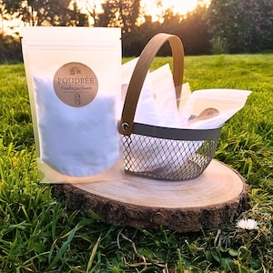 Könnte beinhalten: Ein weißes Pulver in einem durchsichtigen Plastikbeutel mit einem braunen Etikett, auf dem "Poudrée" und "Poudre parfumée" steht. Der Beutel liegt auf einer Holzscheibe neben einem grauen Drahtkorb, der mit weiteren Beuteln mit weißem Pulver gefüllt ist.