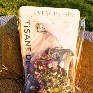 Puede incluir: Una bolsa de plástico transparente que contiene una mezcla de té de hojas sueltas llamada "TISANE DE EAT" con el texto "ENERGISE-MOI EAU ROSEE CITRON, MENTHE, POIVRE 28 G" en el empaque. La mezcla de té contiene pétalos de rosa secos, hojas de menta y otras hierbas.