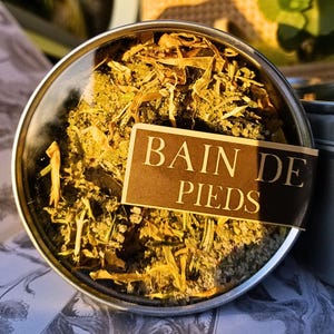 Könnte beinhalten: Eine silberne Dose mit einem durchsichtigen Deckel, gefüllt mit getrockneten Kräutern und Blumen. Das Etikett auf der Dose lautet "Bain de Pieds".