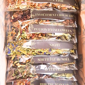 Könnte beinhalten: Eine Schachtel mit mehreren transparenten Beuteln mit losem Blatttee. Jeder Beutel hat ein braunes Etikett mit goldenem Text. Die Etiketten lauten "Tea-Time", "Envoûtement Chocolat", "Potion D'Halloween", "Night", "Sortilège de Noël", "After Light" und "Philtre D'Antan".