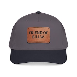 May include: A gray baseball cap with a navy blue brim. A brown leather patch on the front displays the text "FRIEND OF BILL W." in capital letters. The cap has a curved brim and a button on top.