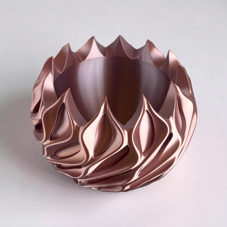 A 3D‑printed planter with a curvy cylindrical form, featuring bold vertical chunky wavy ridges that twist elegantly from top to bottom. The pot includes drainage holes and comes with a matching drip tray that mirrors the same sculptural surface design. Made from glossy Rose Gold Silk PLA, the planter has a luminous sheen that enhances its contemporary art aesthetic.