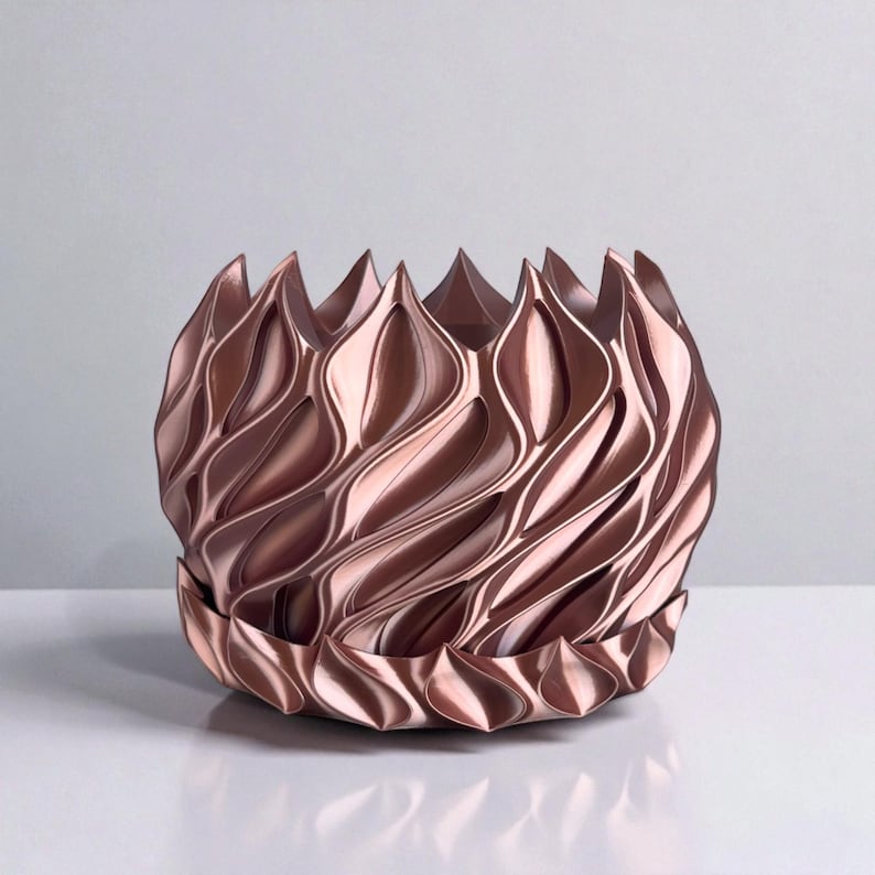 A 3D‑printed planter with a curvy cylindrical form, featuring bold vertical chunky wavy ridges that twist elegantly from top to bottom. The pot includes drainage holes and comes with a matching drip tray that mirrors the same sculptural surface design. Made from glossy Rose Gold Silk PLA, the planter has a luminous sheen that enhances its contemporary art aesthetic.