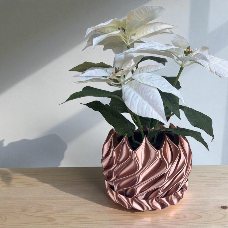 A 3D‑printed planter with a curvy cylindrical form, featuring bold vertical chunky wavy ridges that twist elegantly from top to bottom. The pot includes drainage holes and comes with a matching drip tray that mirrors the same sculptural surface design. Made from glossy Rose Gold Silk PLA, the planter has a luminous sheen that enhances its contemporary art aesthetic.
