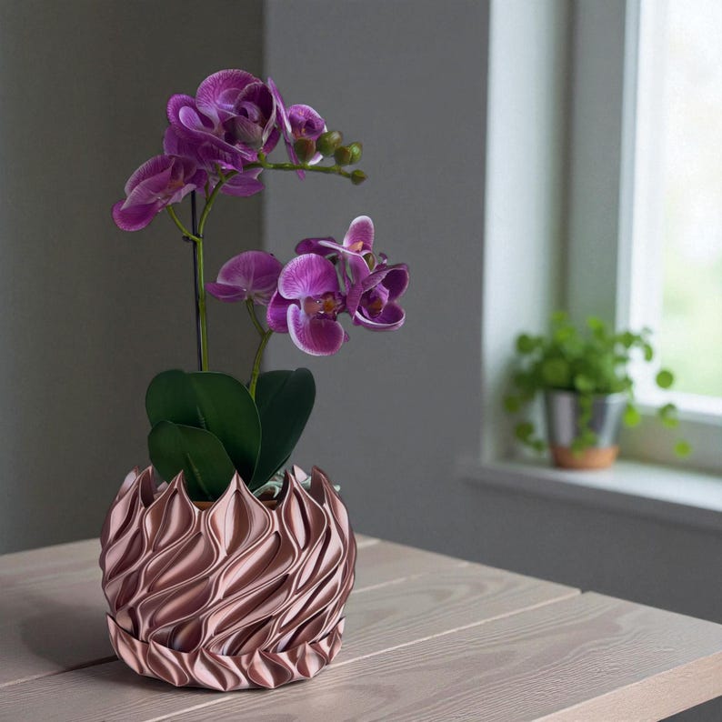 A 3D‑printed planter with a curvy cylindrical form, featuring bold vertical chunky wavy ridges that twist elegantly from top to bottom. The pot includes drainage holes and comes with a matching drip tray that mirrors the same sculptural surface design. Made from glossy Rose Gold Silk PLA, the planter has a luminous sheen that enhances its contemporary art aesthetic.