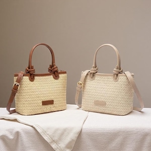 May include: Two straw handbags with leather accents. One bag has brown leather trim, handles, and a shoulder strap. The other bag has beige leather trim, handles, and a shoulder strap. Both bags have a rectangular shape and a small rectangular leather patch.