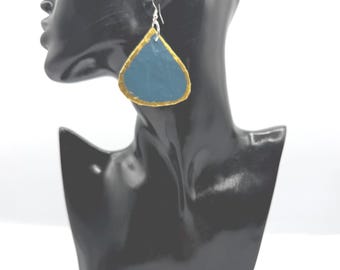 May include: A teardrop-shaped earring featuring a matte blue center surface with a textured gold-painted border. The earring hangs from a silver-toned metal hook, displaying a distinct contrast between the blue interior and the metallic gold edge.
