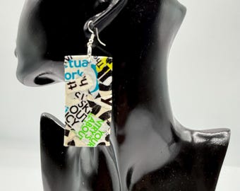 May include: A rectangular dangle earring featuring a collage of black, white, blue, and green printed paper text. The earring is suspended from a silver-toned metal hook and displays fragmented words including 'work', 'out', and 'about' on its surface.